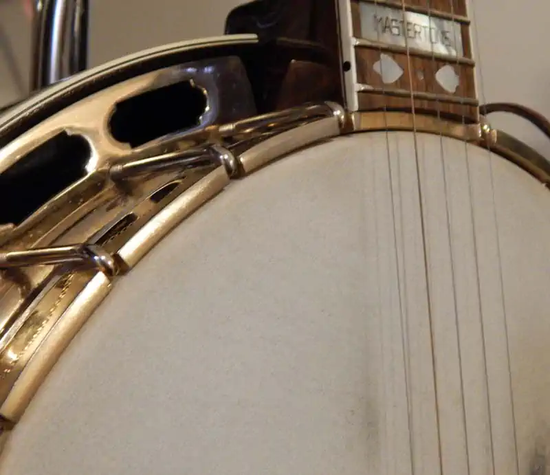 Close-up view of a Gibson Mastertone banjo drum head, tension hoop, metal tone ring, and fretboard inlays.