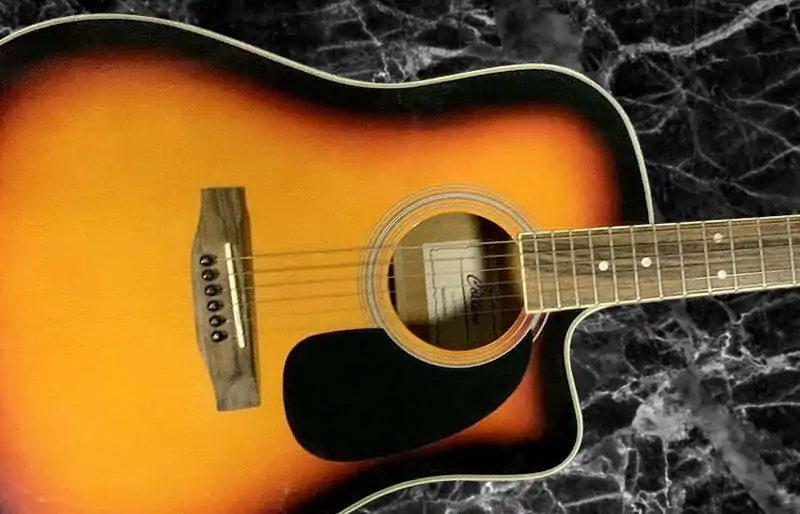 Collings acoustic guitar setup, repair, and servicing in London Sunburst cutaway dreadnought acoustic guitar body resting on a dark marble background.