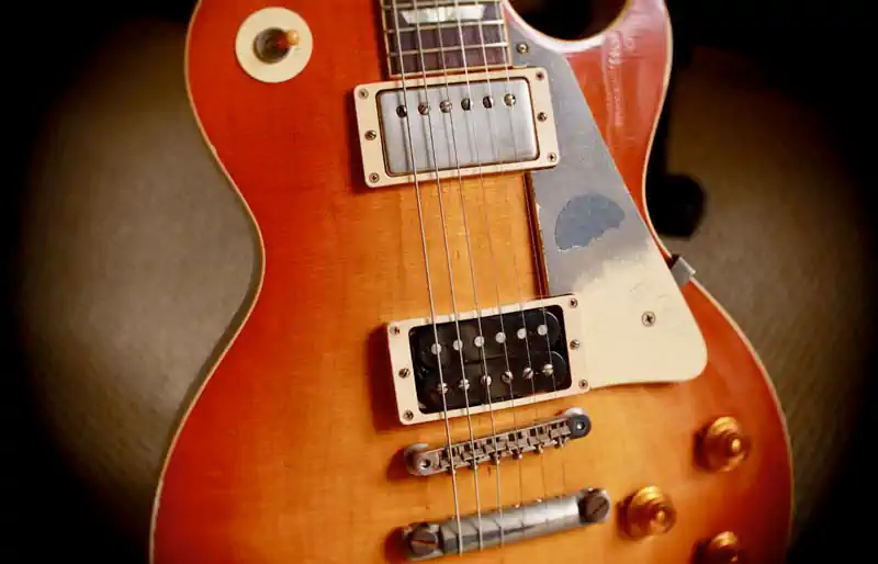 Gibson Les Paul sunburst body with dual humbuckers, Tune-o-matic bridge, pickup selector, and pickguard close-up.
