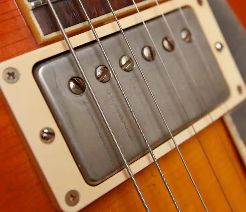 Close-up of a chrome humbucker pickup, strings, and mounting ring on a sunburst electric guitar.