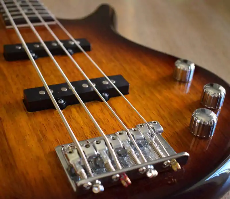 An angled close-up view of a four-string Ibanez bass guitar featuring a sunburst finish, dual single-coil pickups, chrome bridge, and metallic control knobs on a wooden surface.