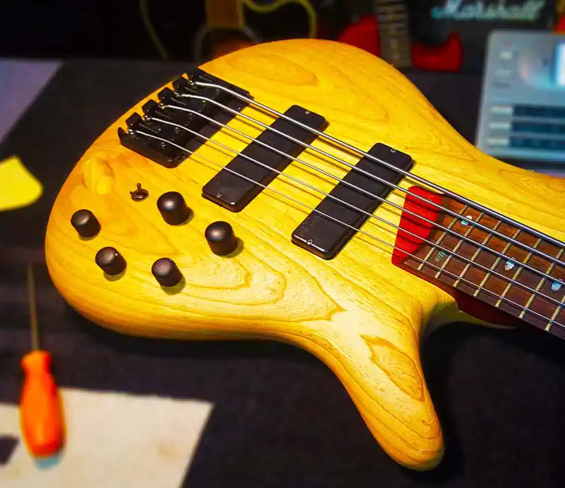 Natural finish wood body of an Ibanez five-string electric bass guitar with pickups, knobs, and bridge on a workbench.