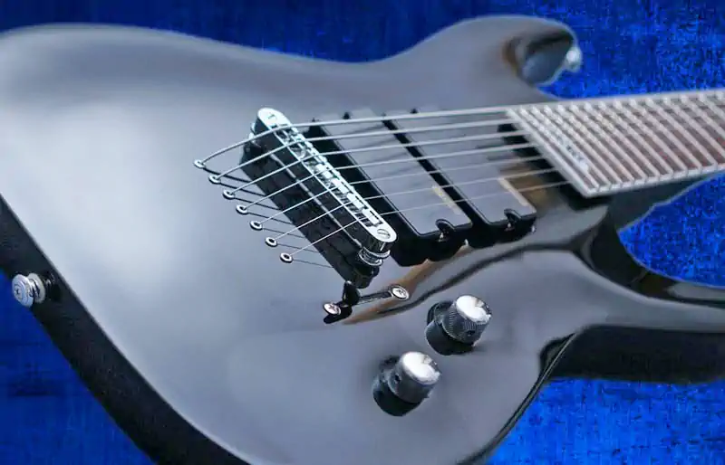 Black 7-string ESP LTD electric guitar body showing string-through bridge, dual pickups, and knobs on a blue fabric background.