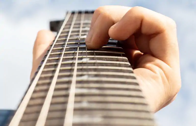 Low-angle view looking down a PRS rosewood fretboard with bird inlays as a hand frets notes against a sky background.