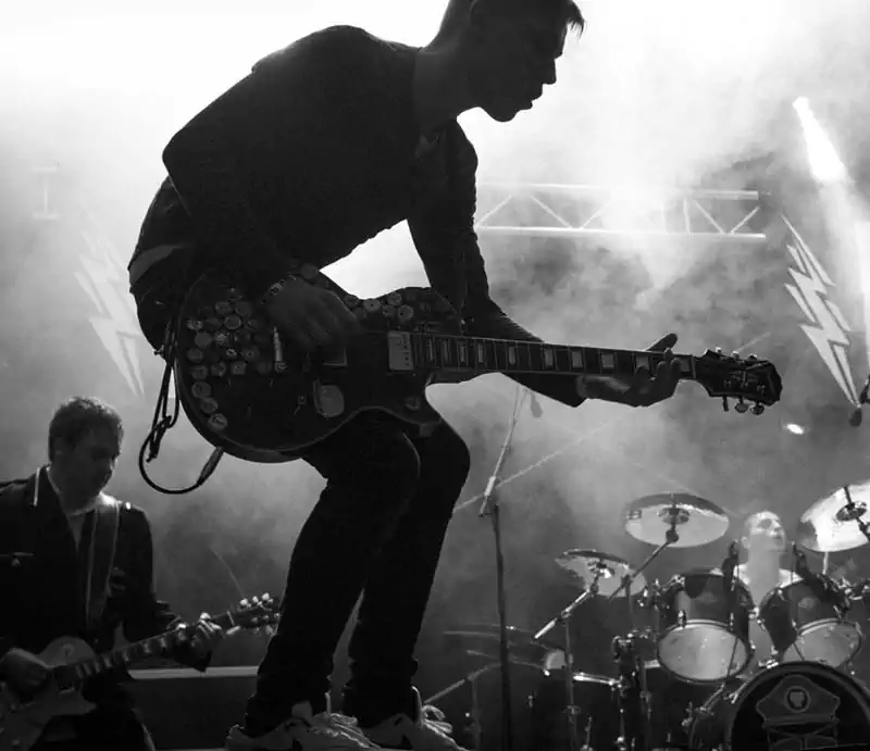 Monochrome photo of a rock guitarist performing live on stage surrounded by smoke and stage lights.