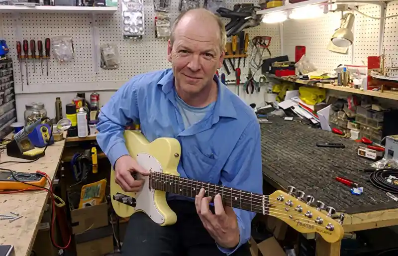 Tim Marten holding and testing a Fender Telecaster style guitar in his workshop.