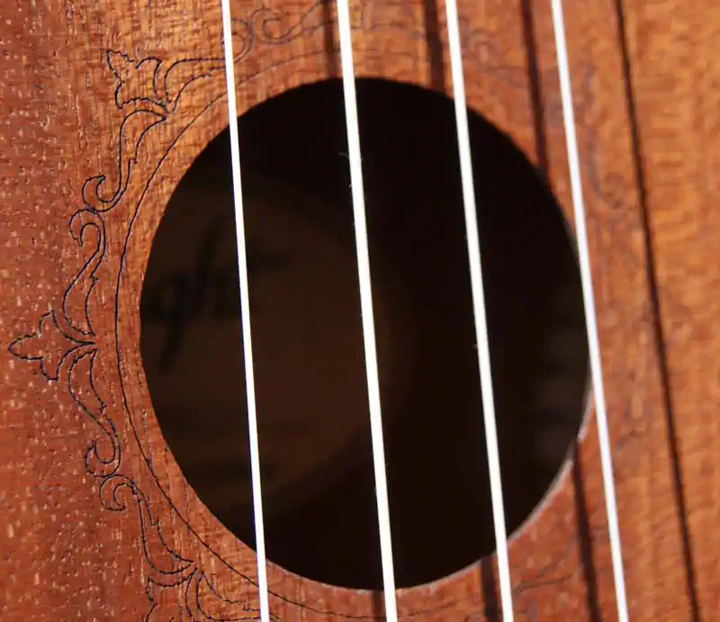 Close-up of a wooden Flight ukulele soundhole showing engraved laser rosette pattern detail and nylon strings.