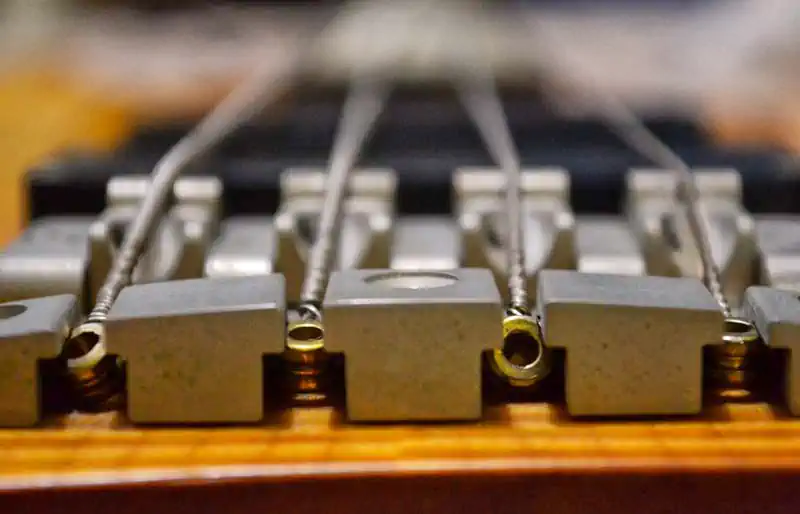 Bass guitar repair & servicing Macro shot looking down the metal bridge saddles and ball-end strings of a 4-string electric bass guitar with wood finish.